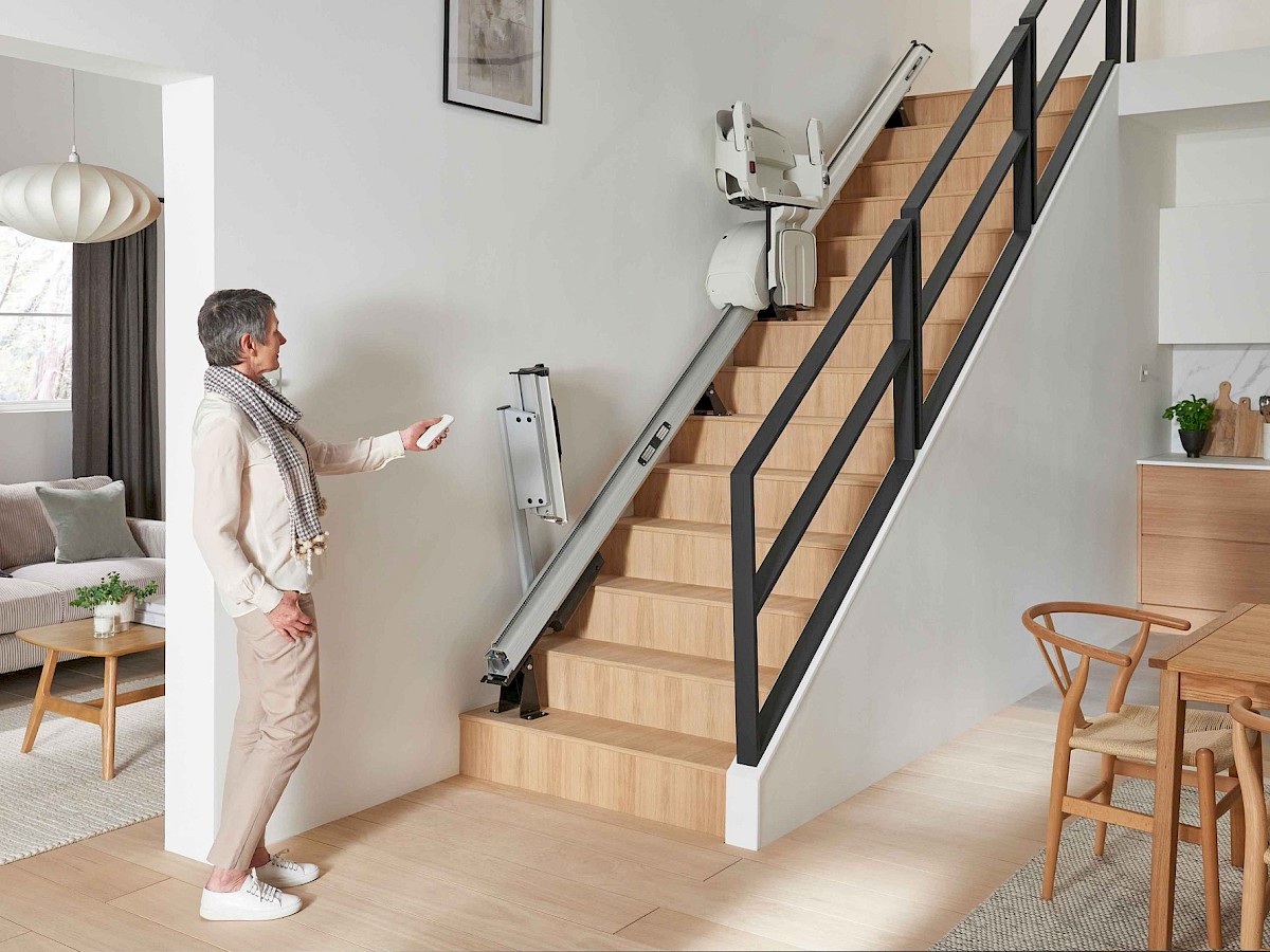 Frau bedient mit der Fernbedienung einen Sitzlift an einer geraden Treppe im Wohnbereich