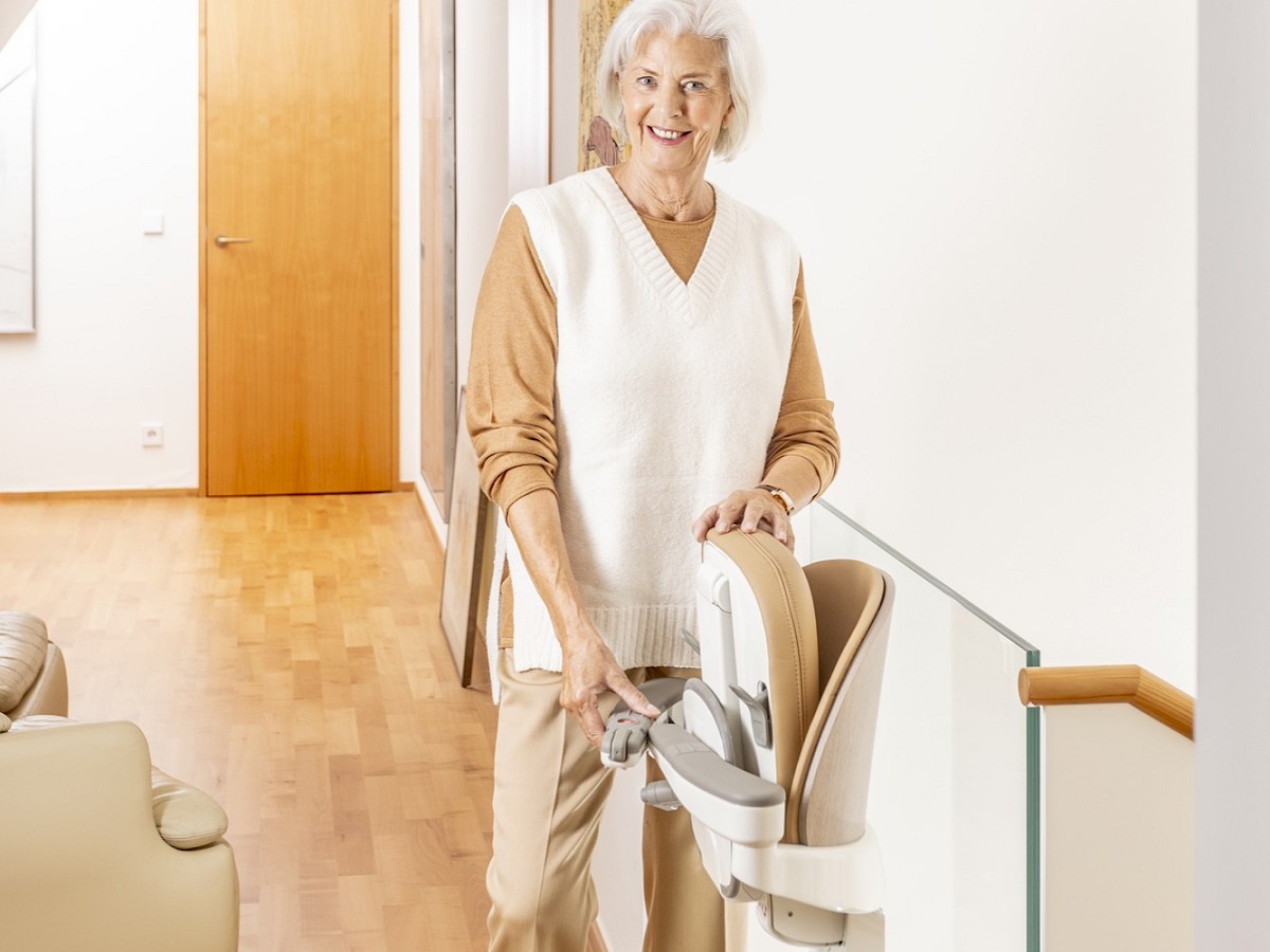 &Auml;ltere Dame steht neben einem Sitzlift im Flur eines Wohnhauses