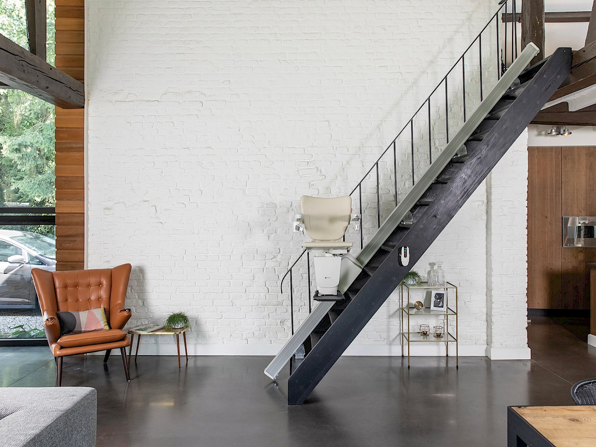Sitzlift an einer schmalen Treppe mit schwarzem Stahlgel&auml;nder in einem hellen Wohnraum