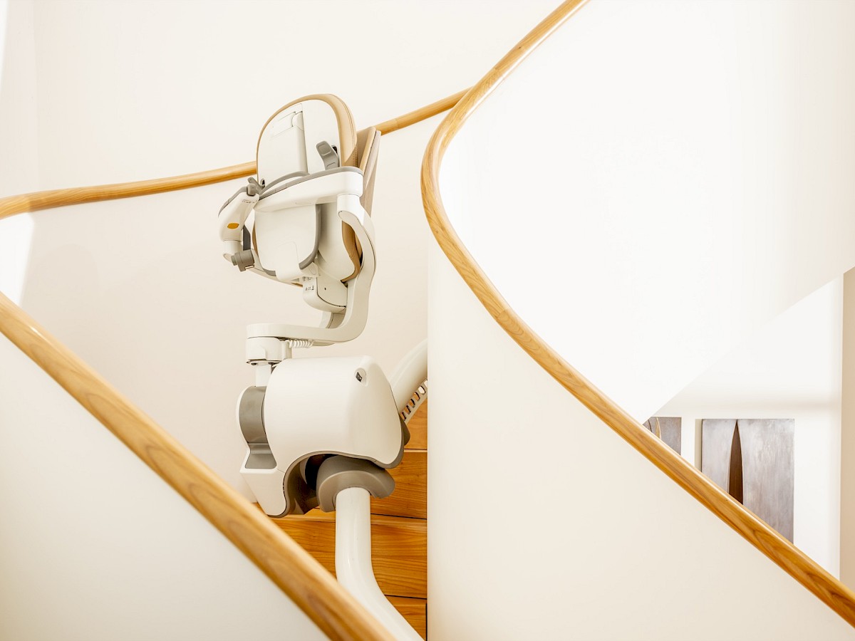 Sitzlift auf der Schiene einer geschwungenen Treppe mit Holzhandlauf