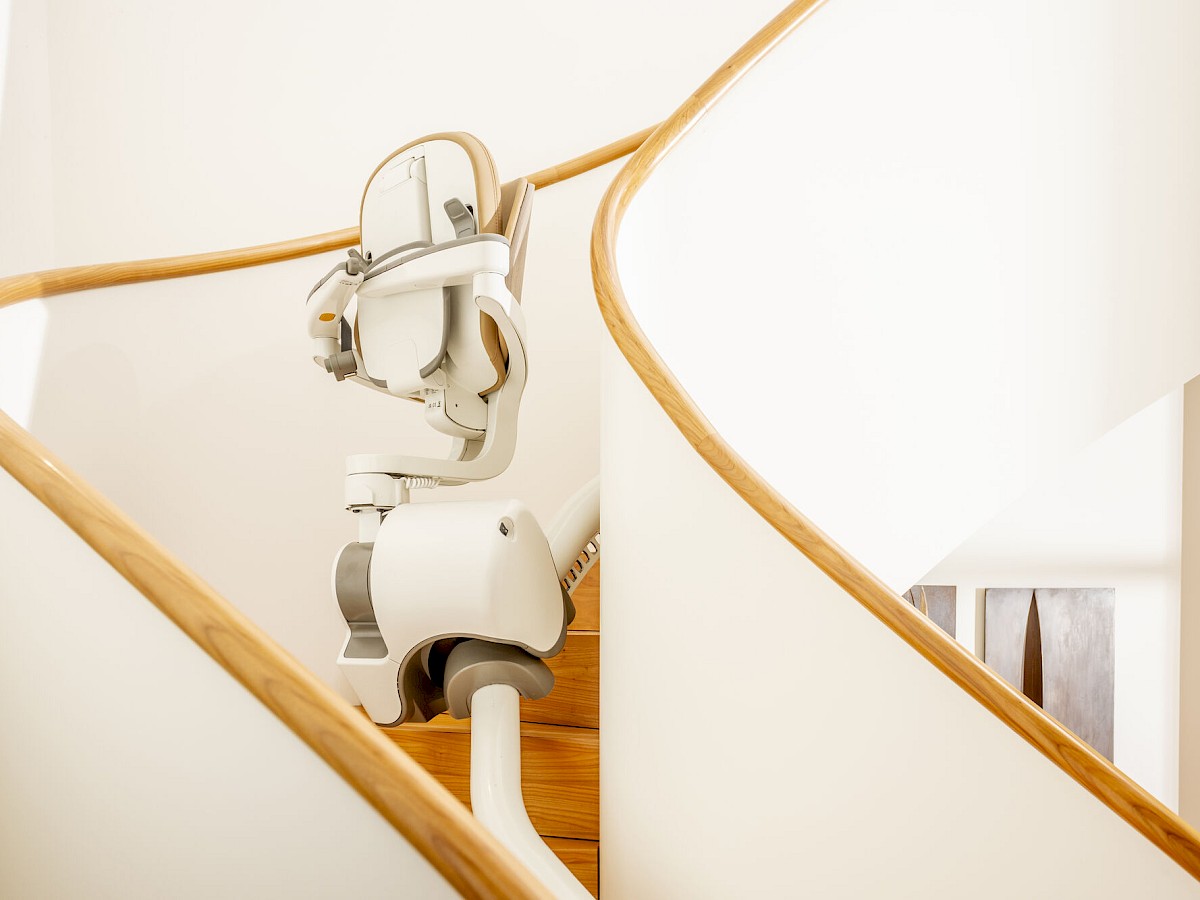 Ma&szlig;gefertigte Schiene mit Sitzlift Flow SL folgt dem Verlauf einer geschwungenen Treppe