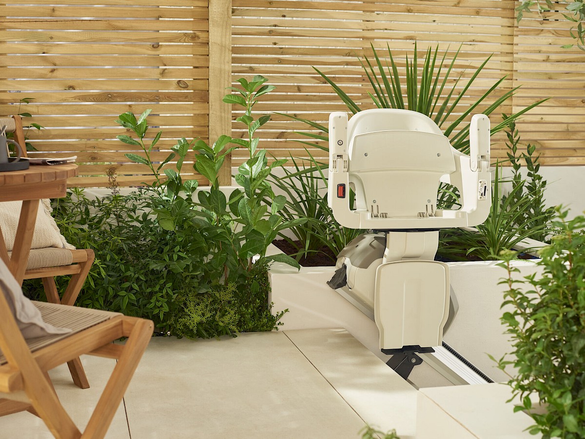 Sitzlift SL Outdoor mit hellem Sitz auf einer Terrasse zwischen Pflanzen